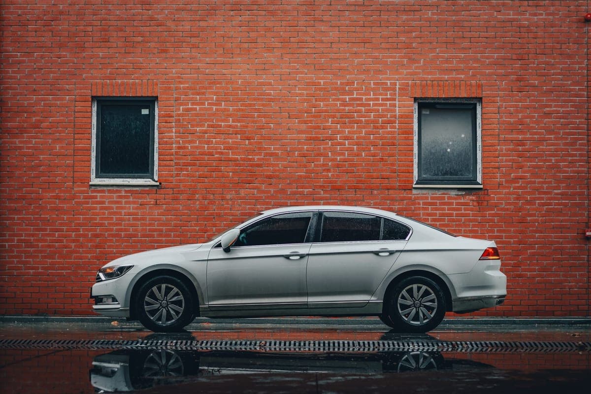 2019 Volkswagen Passat SE in Pure White, clean side profile against a red brick wall on wet pavement