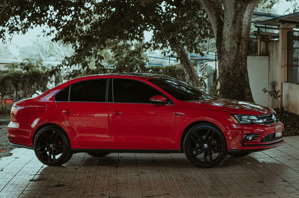 2019 Volkswagen Jetta GLI in Tornado Red with black alloy wheels, side profile under a shade tree