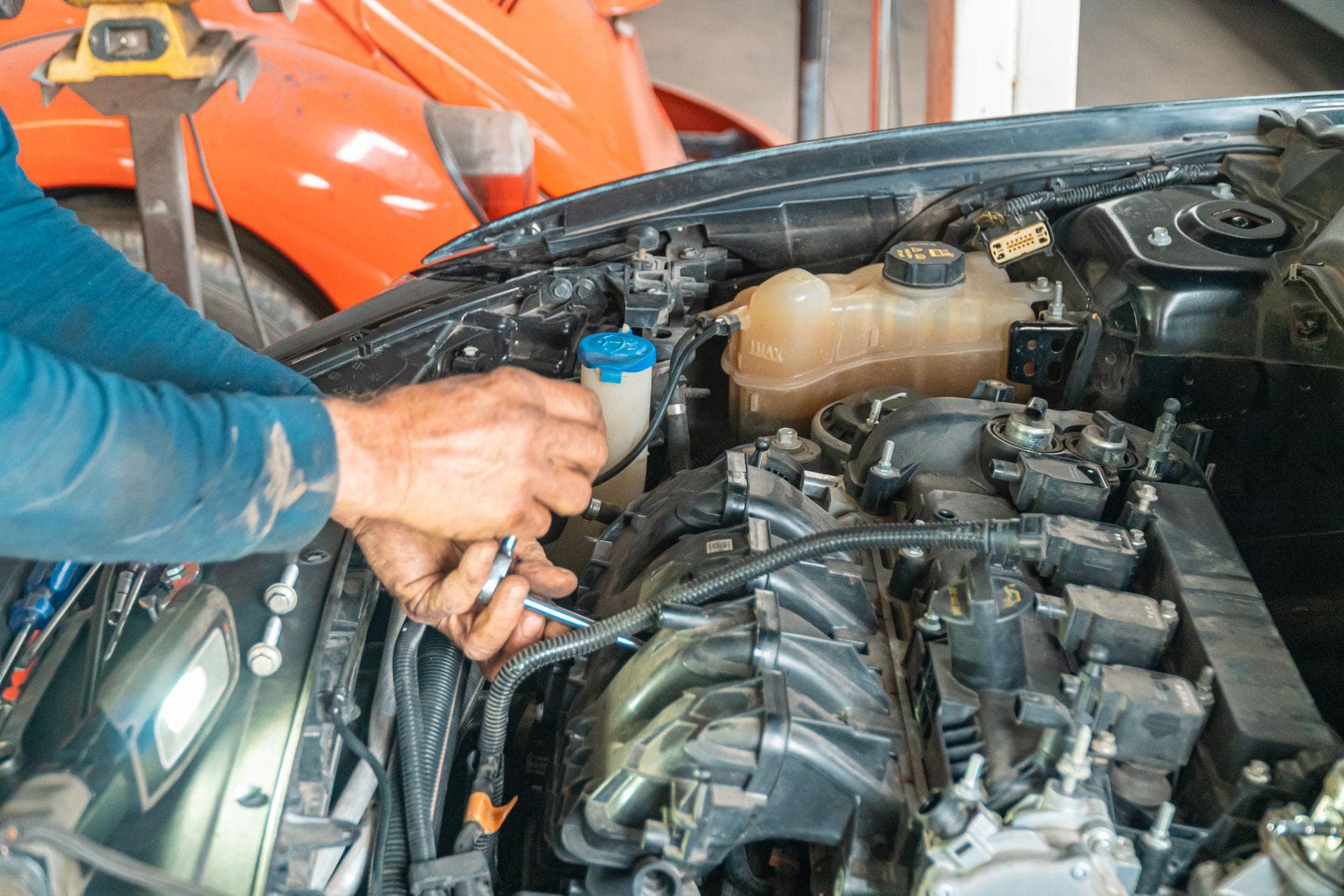 A technician's hands on a wrench deep in an engine bay